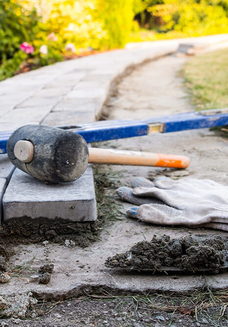 Masonry tools, a rubber mallet, and a mortar trowel sitting on a custom brick walkway installation in Dearborn Heights