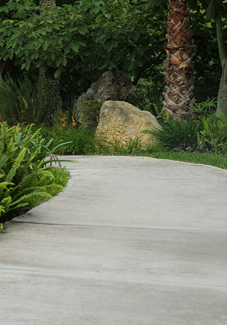 A smooth, curved pedestrian walkway installed by D & G Cement Company in Redford MI through a landscaped backyard garden